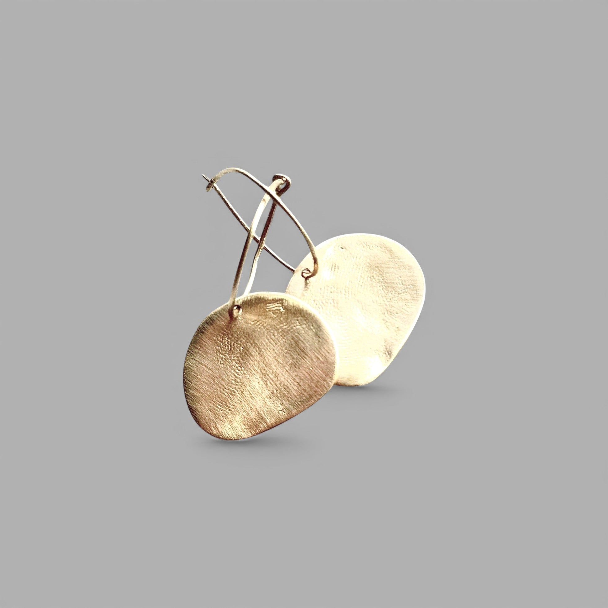 Pendientes en oro mate PM7G de la colección Martina sobre un fondo liso con reflejos