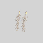 Pendientes en oro mate PB1 de la colección Brisa sobre un fondo de color