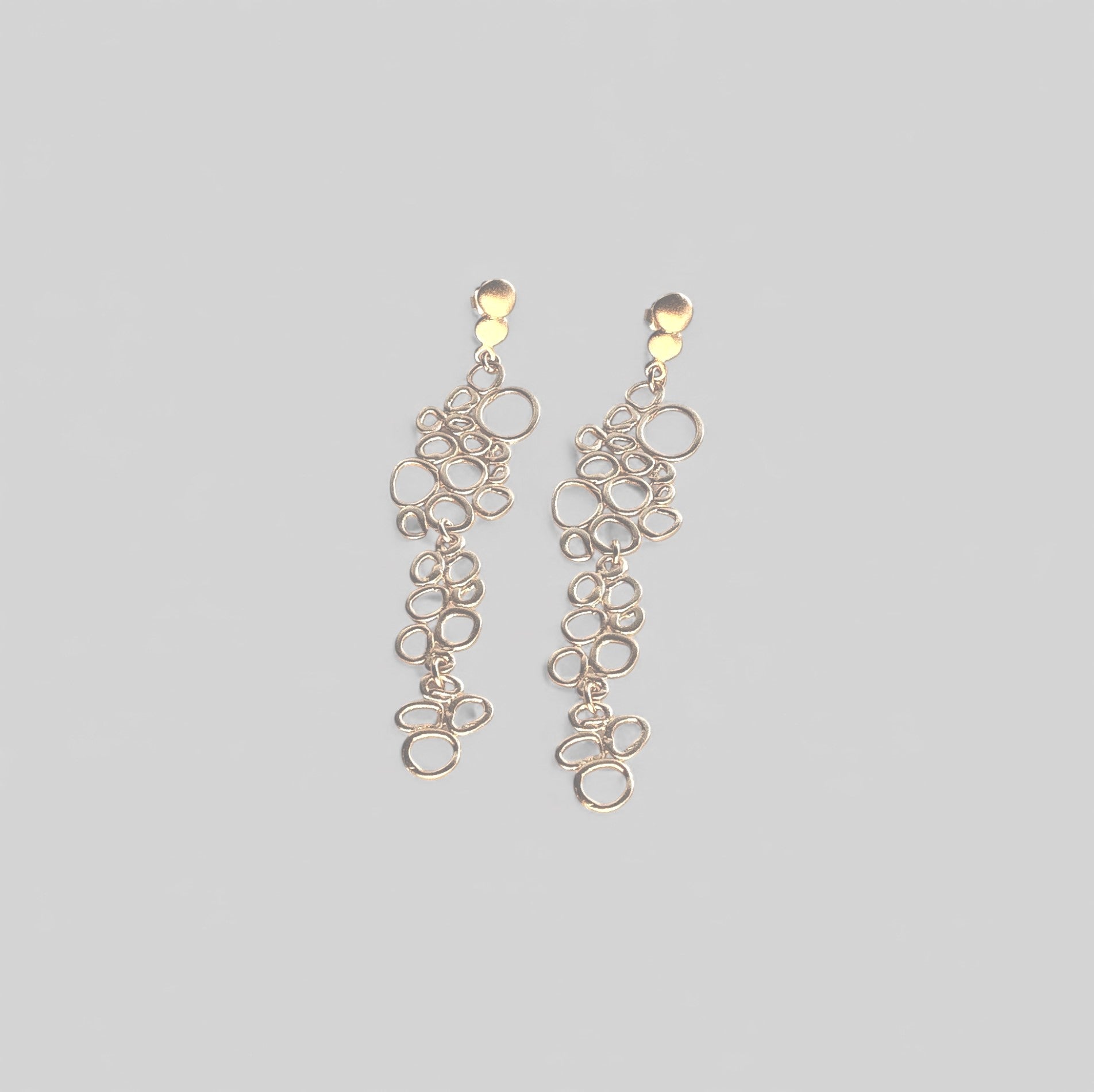 Pendientes en oro mate PB1 de la colección Brisa sobre un fondo de color